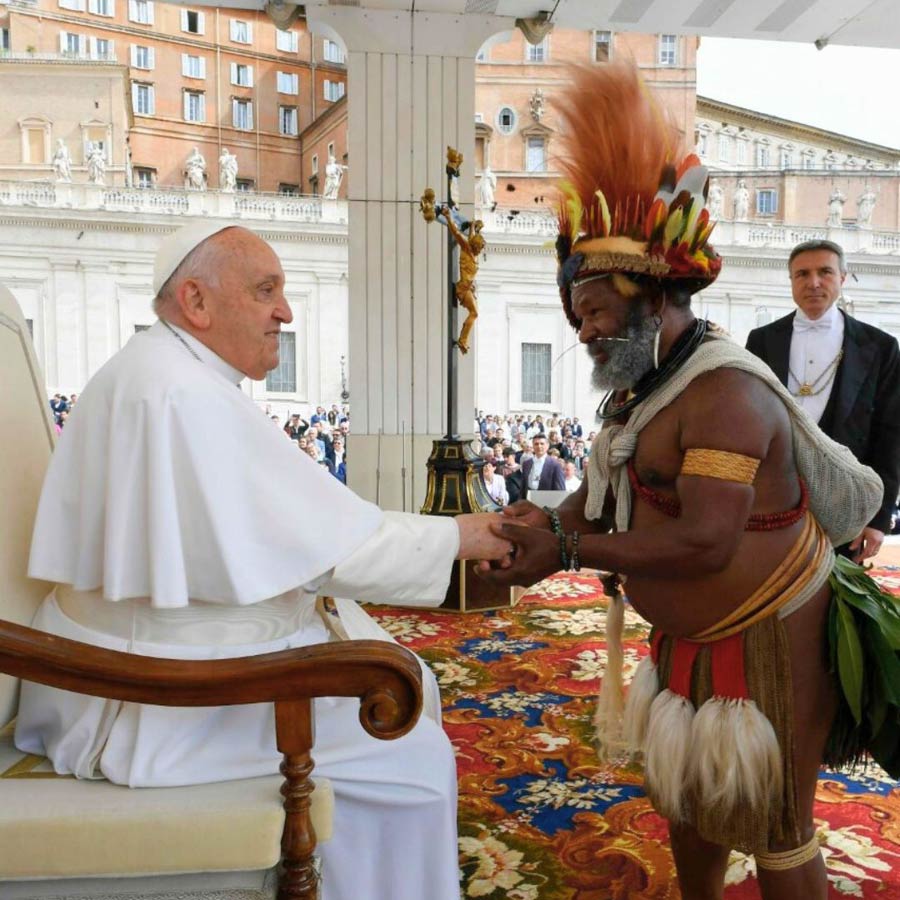 Der in abenteuerlich erscheinender Stammestracht gekleidete Ehrengast reicht dem Papst die Hand