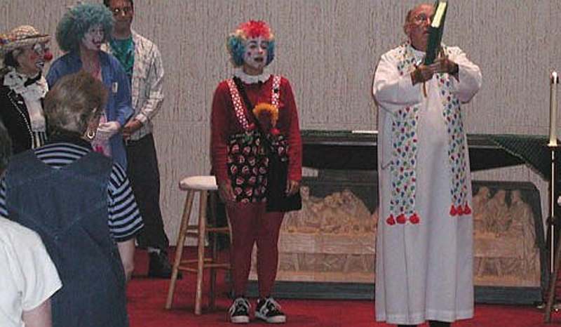 Bischof Frank Devane bei einer Clowns-Messe 2008 in Sarrasota <br>Bild: https://www.calefactory.org/ Bischof in Albe und Clowns-Stola umstanden von konzelebrierenden (?) Priestern in Clownskostümen