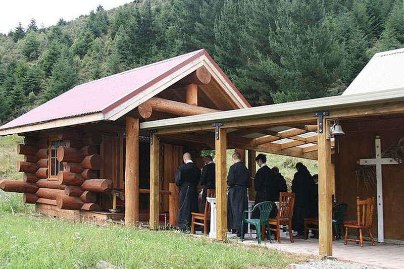 Kapelle des Stützpunktes der FSSR in Christchurch, Neuseeland
                               <br>Bild: Website der FSSR Die Kapelle des Stützpunktes der FSSR in Christchurch, Neuseeland und das daneben teilweise sichtbare Wohnhaus sind als Blockhäuser ausgeführt. Vor der Kapelle warten einige Brüder auf den Einzug zum Gebet.