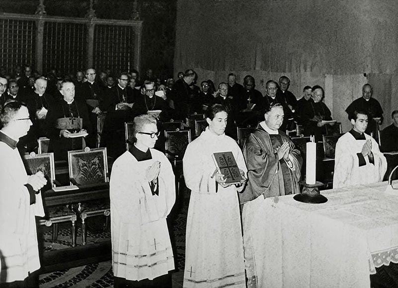 Erzbischof Bugnini und Altardienst zu Beginn der Messfeier. Die Stellung der Leuchter und der ganz rechts sichtbare Fuß eines Mikrophons lassen erkennen, daß die eigentliche Zelebration „ad populum “ stattfand. Von einem Altarkreuz ist nichts zu sehen. Das Photo aus der Sixtinischen Kapelle zeigt Erbuschif Bugnini, zwei Ministranten und einen Lektor unmittelbar vor Beginn der Messe an einem in der Sixtina aufgestellten „Volksaltar“.