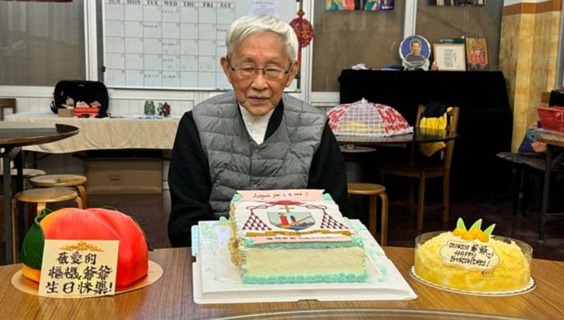 Das  Bild zeigt den Kardinal vor einem Geburtstagstisch mit drei Torten: Rechts und links je eine mit englischer bzw. chinesischer Aufschrift: „Herzlichen Glückwunsch“ in der Mitte eine große rechteckige Torte mit dem Wappen des Kardinals in Zuckerguss.