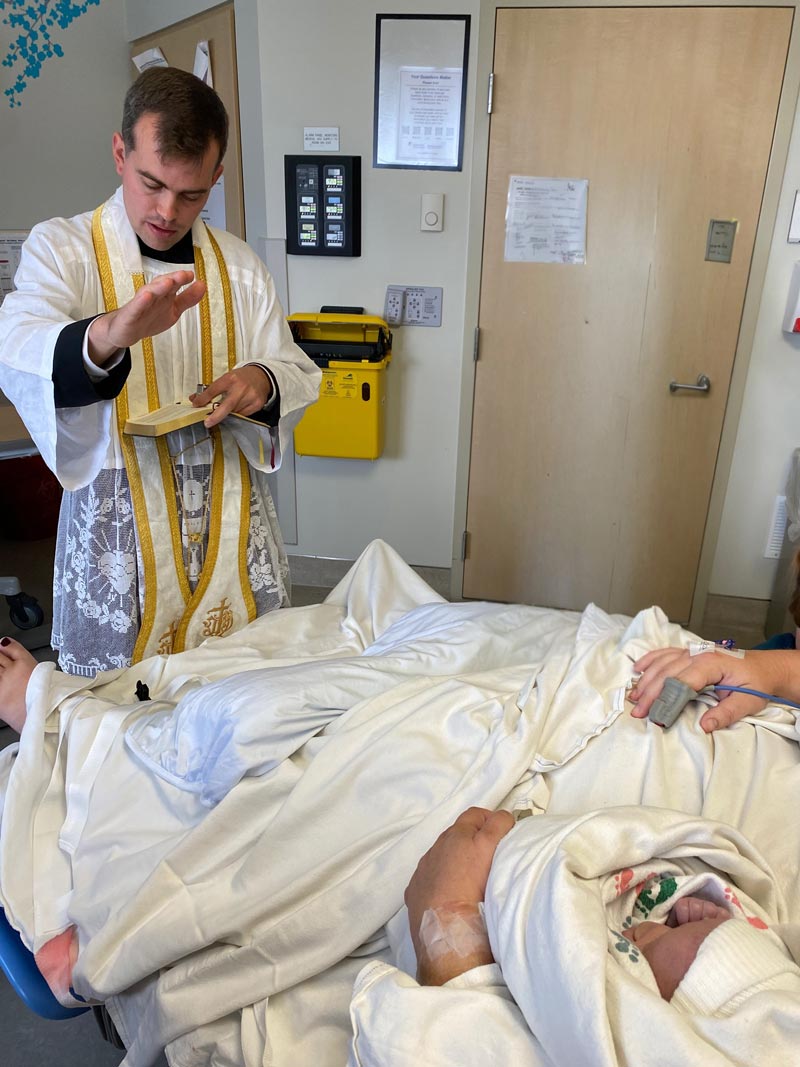 Die Aufnahme zeigt das Krankenbett mit der Frau von Kennedy Hall, die ihren sterbenden Neugeborenen im Arm hält, und am Fußende den Priester bei der Spendung der Sakramente