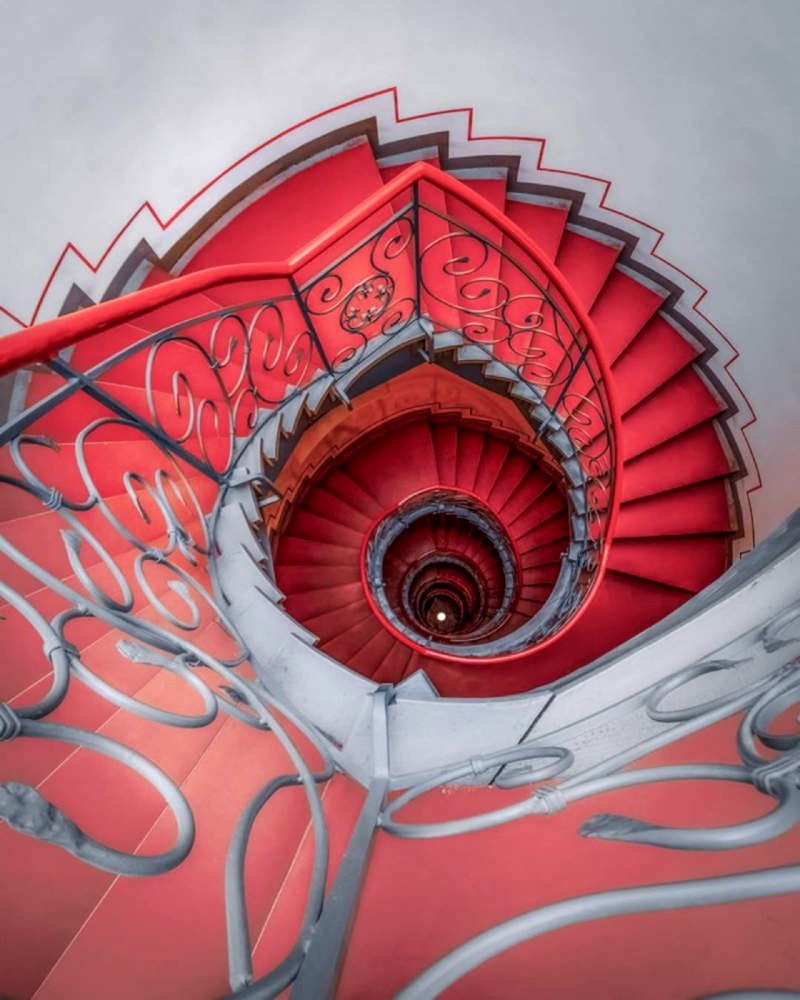 Das Photo zeigt den Blick von oben in ein verwirrend spiralförmiges Treppenhaus in leuchtenden Farben.
